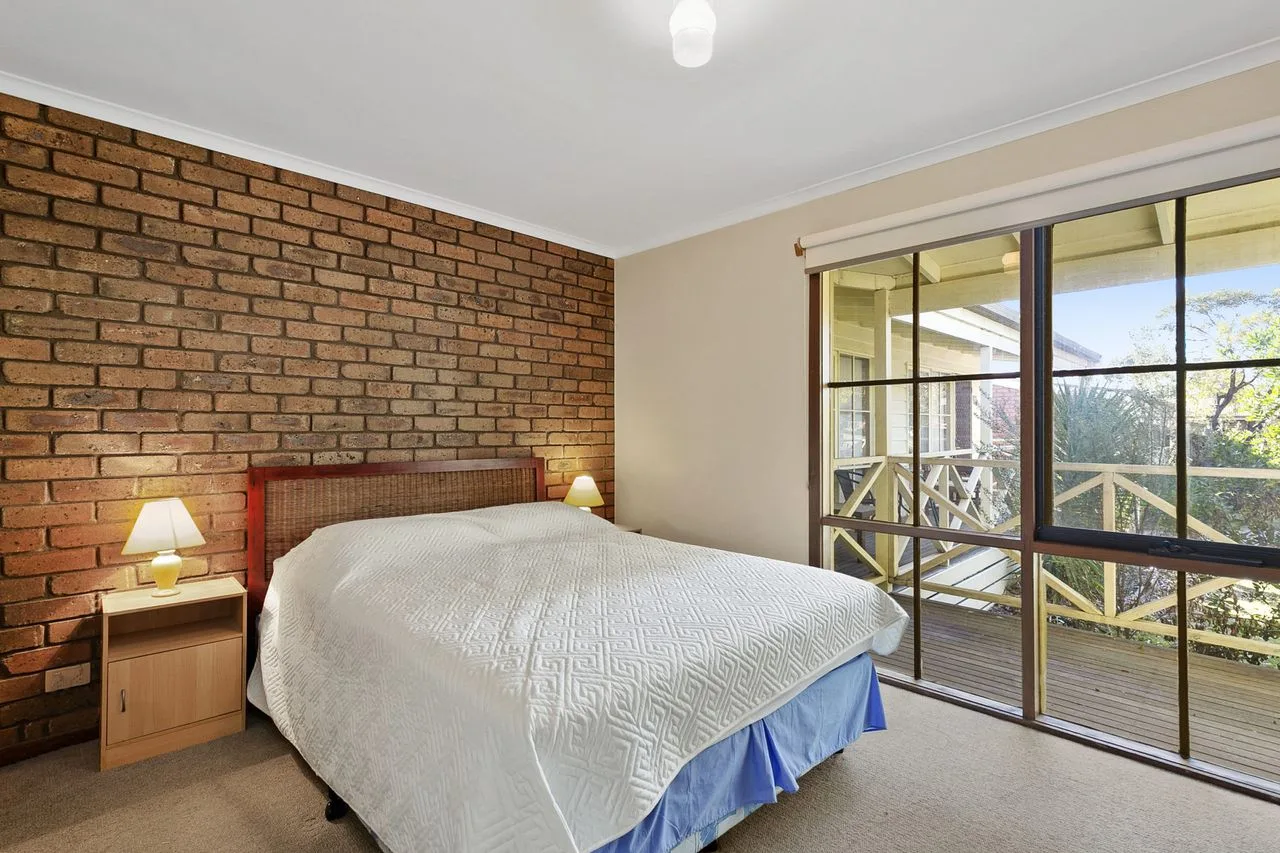 A bedroom with a bed beside a brick wall and large glass doors.