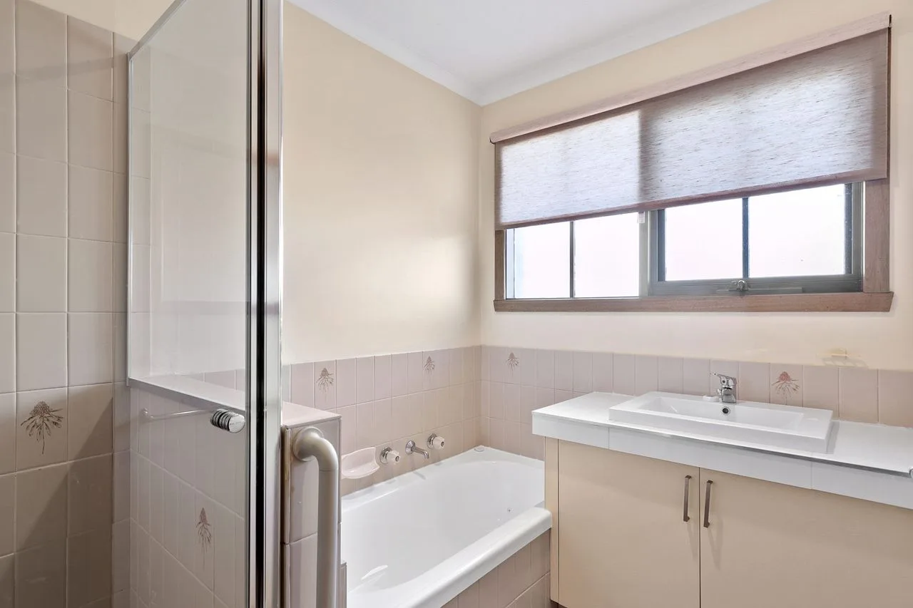Un baño con bañera, ducha y lavabo bajo una ventana.