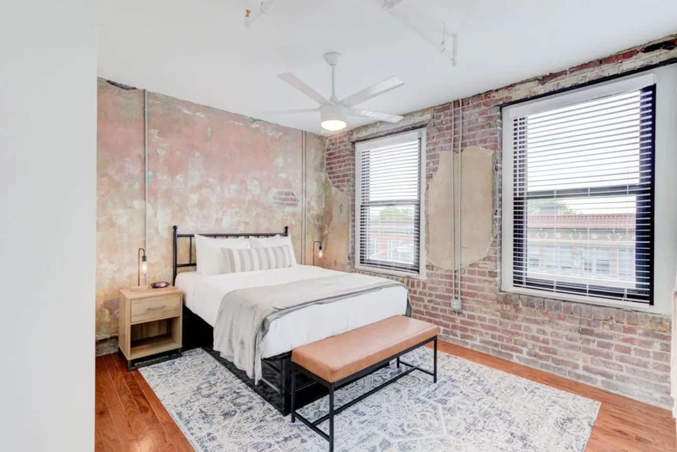 Un dormitorio con una cama, un banco y ventanas grandes.