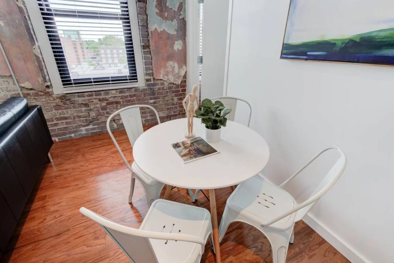 Un pequeño comedor tiene una mesa redonda, asientos blancos y una planta en maceta.