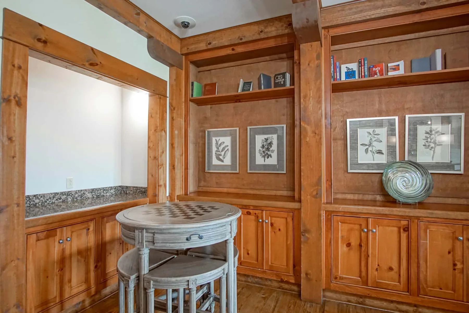 A wood-paneled room with built-in cabinets, framed prints, and a round table.
