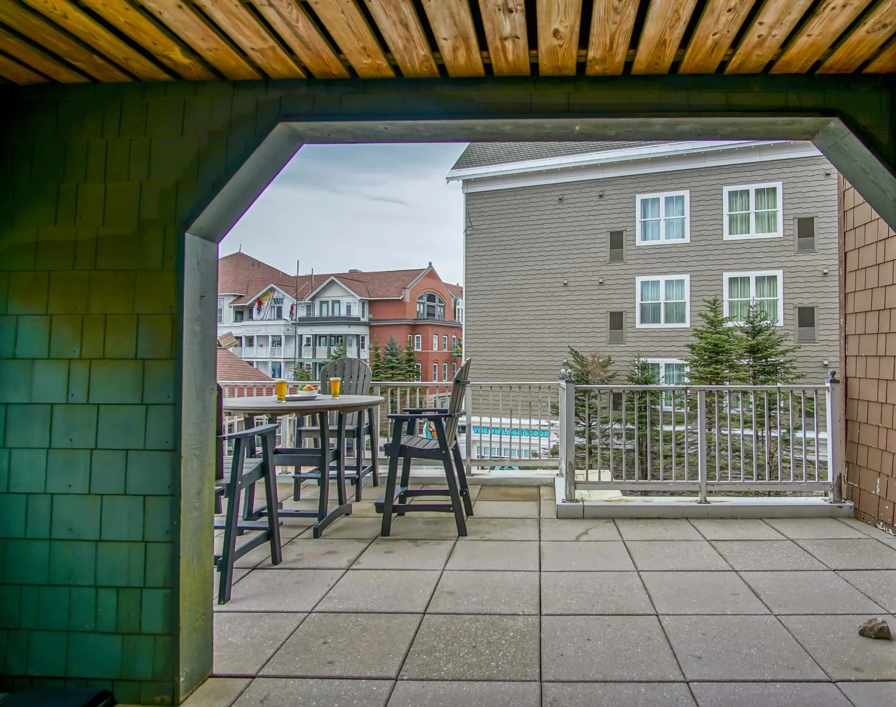 A covered outdoor patio with seating and a railing overlooking nearby buildings.