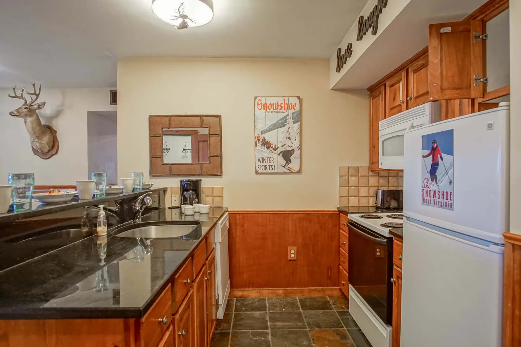A kitchen with dark counters, wooden cabinets, and a refrigerator.