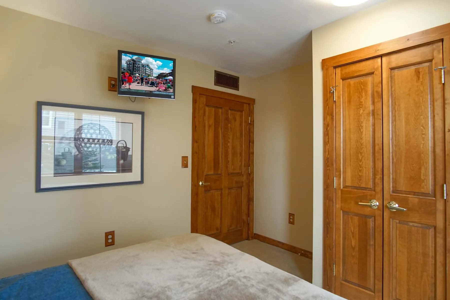 A bedroom with a bed, framed picture, television, and wooden doors.