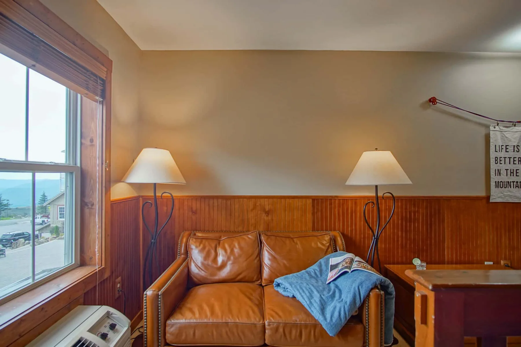 A living room with a leather sofa, two lamps, and a window overlooking the street.