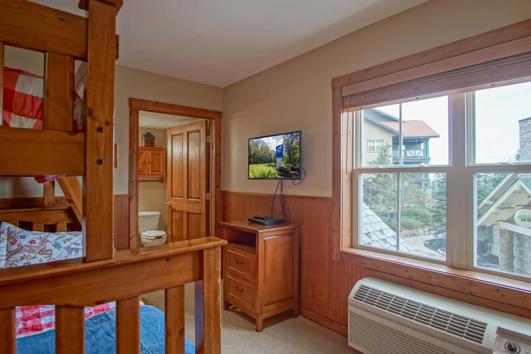 A bedroom with wooden bunk beds, a television, and a large window.