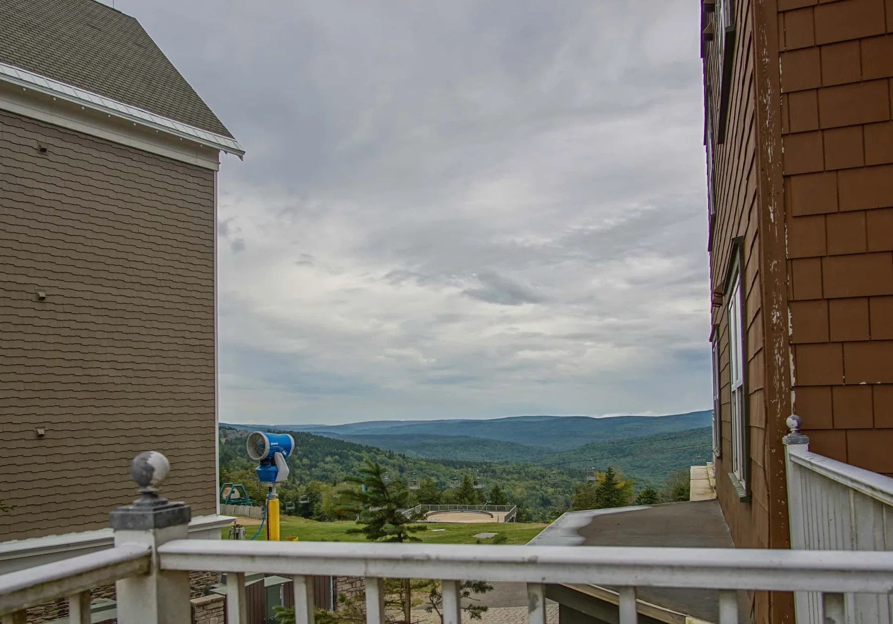 An outdoor balcony overlooks a broad, tree-covered valley beneath a cloudy sky.