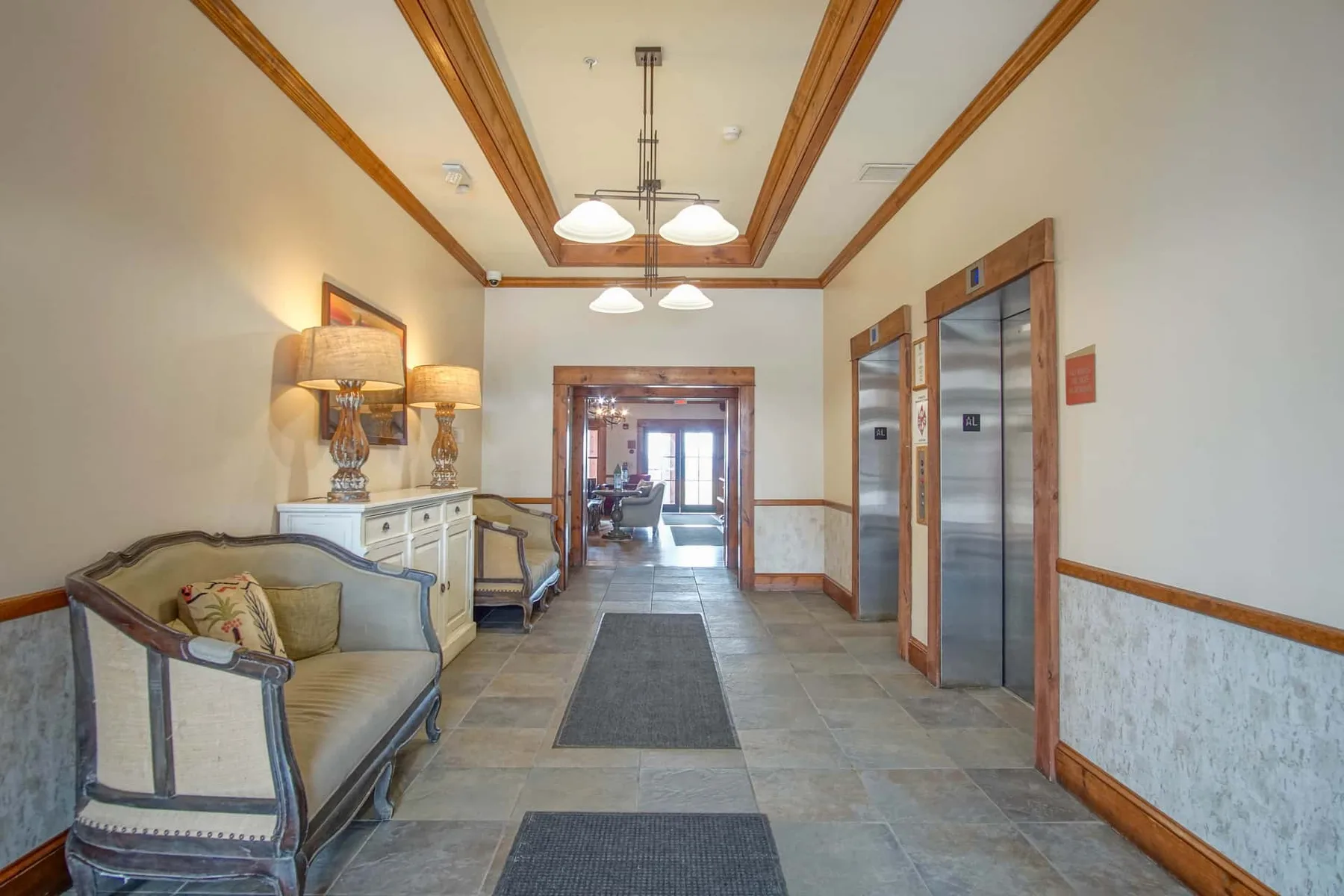 An interior hallway with seating and elevator doors along one side.