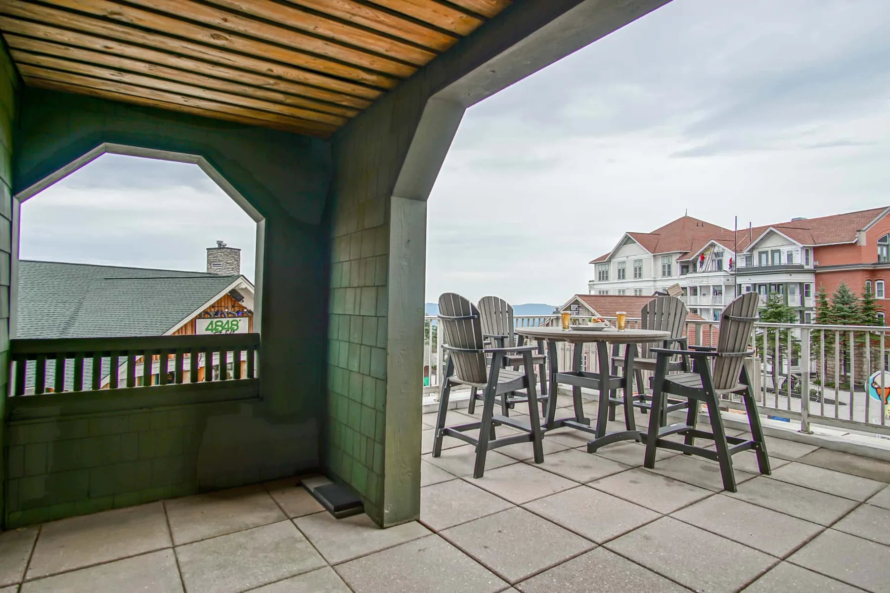 A covered outdoor patio with a dining table and seating overlooks nearby buildings.