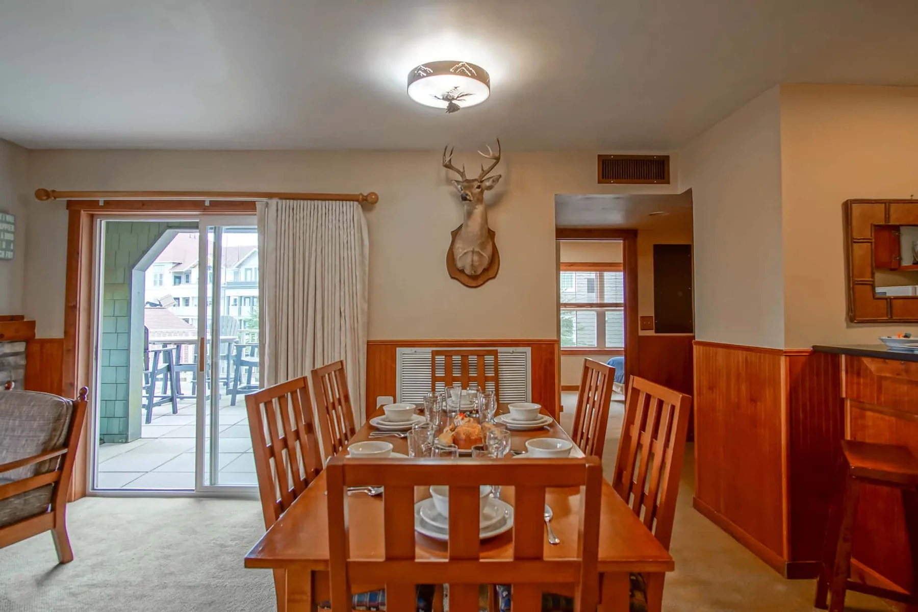 A dining room with a wooden table set for a meal beside a sliding glass door.