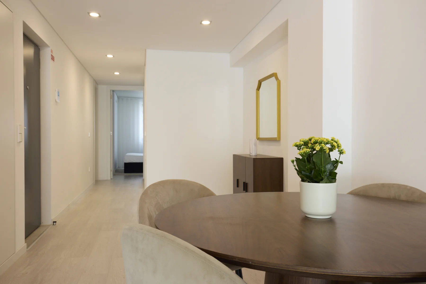A dining area with a round table, chairs, and flowers beside a hallway.