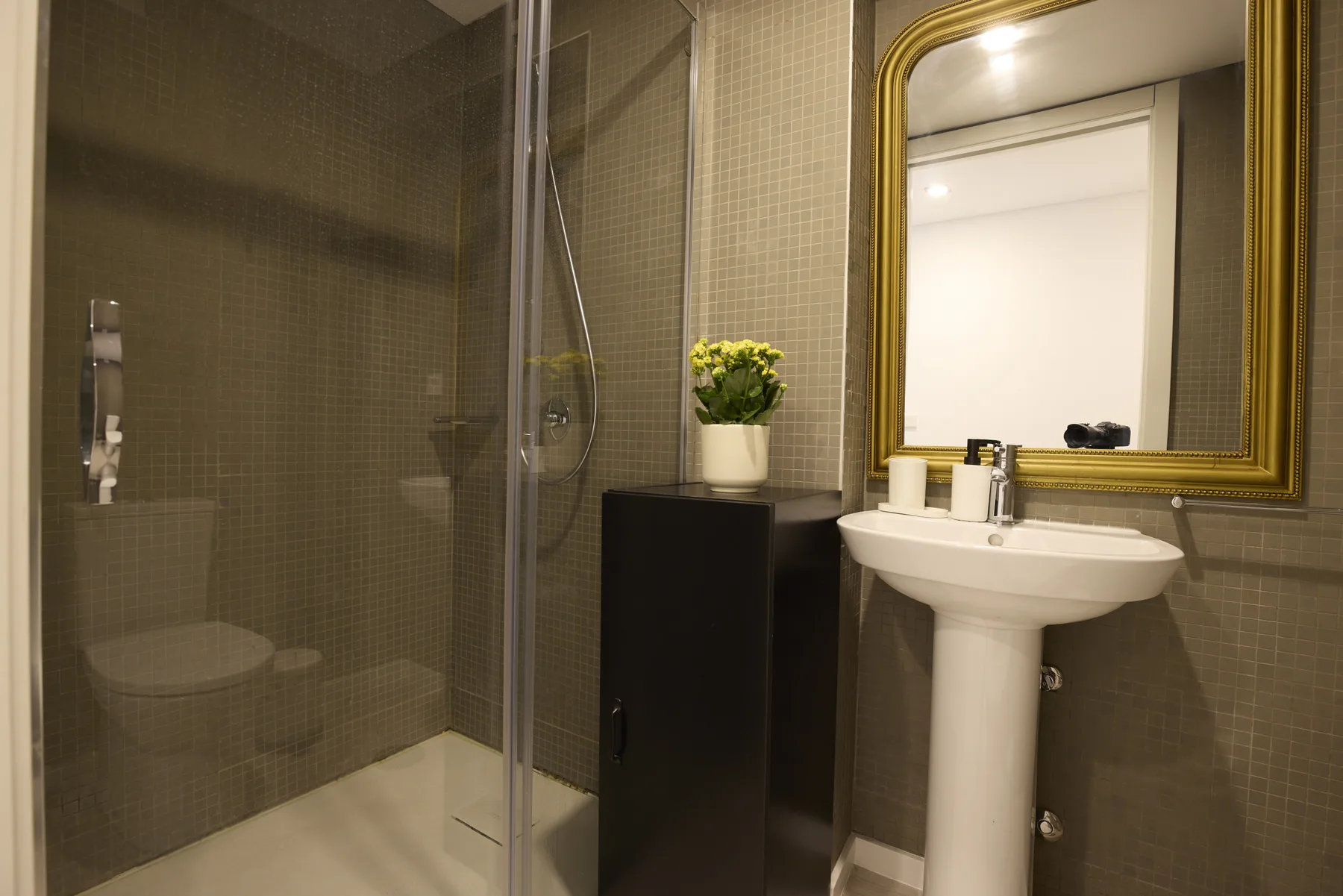 A bathroom with a glass shower, pedestal sink, and wall mirror.