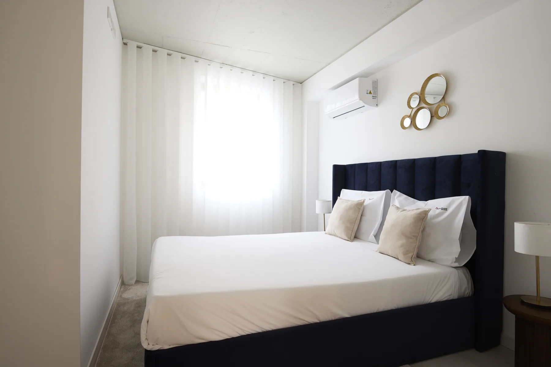 A bedroom with a bed and tall dark headboard beside a bright window.