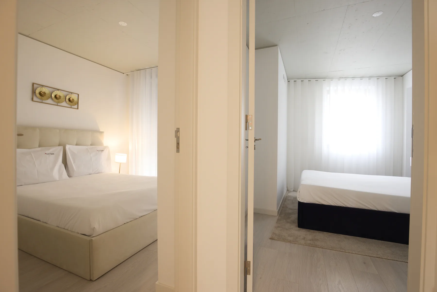 A bedroom with a neatly made bed and a bright curtained window.