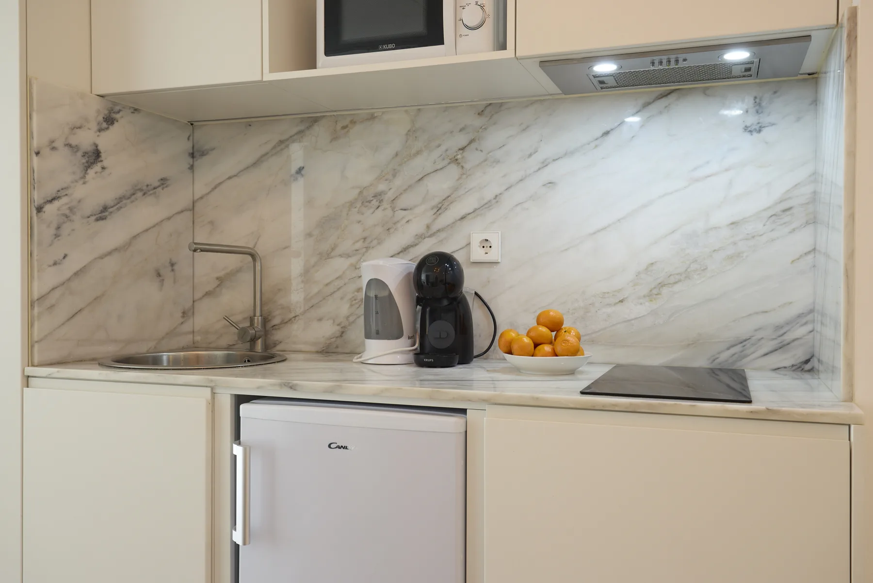 A compact kitchen counter with a sink, small appliances, and a bowl of oranges.