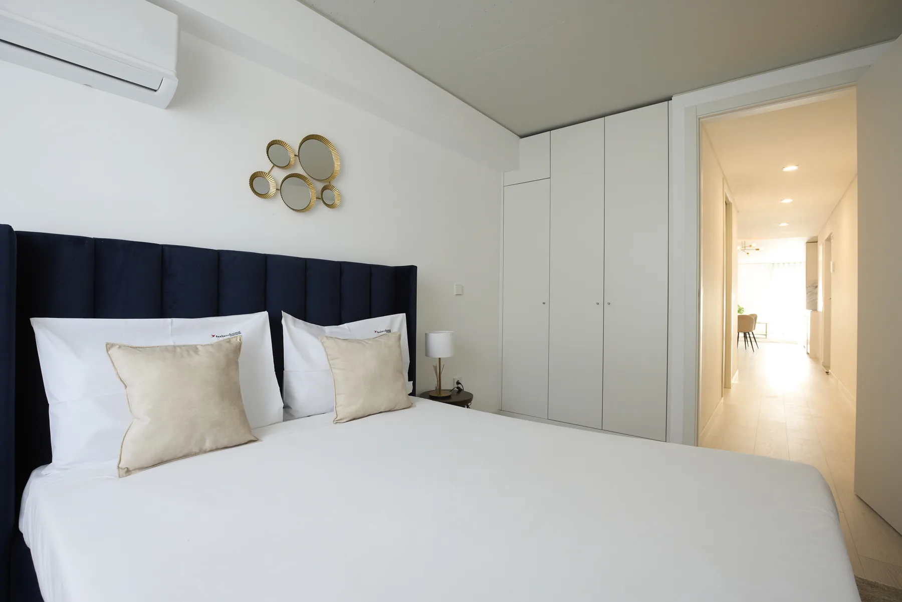 A bedroom with a neatly made bed, white bedding, and a dark upholstered headboard.