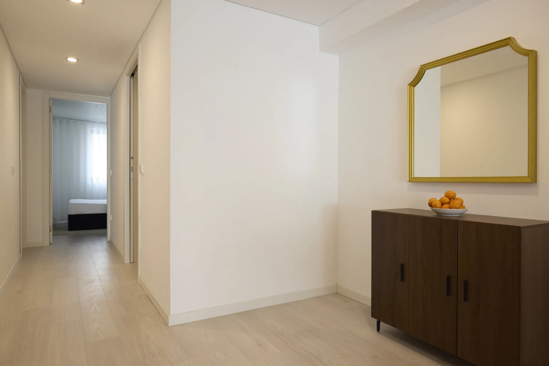 A bright hallway opens toward a bedroom, with a dark cabinet and mirror nearby.
