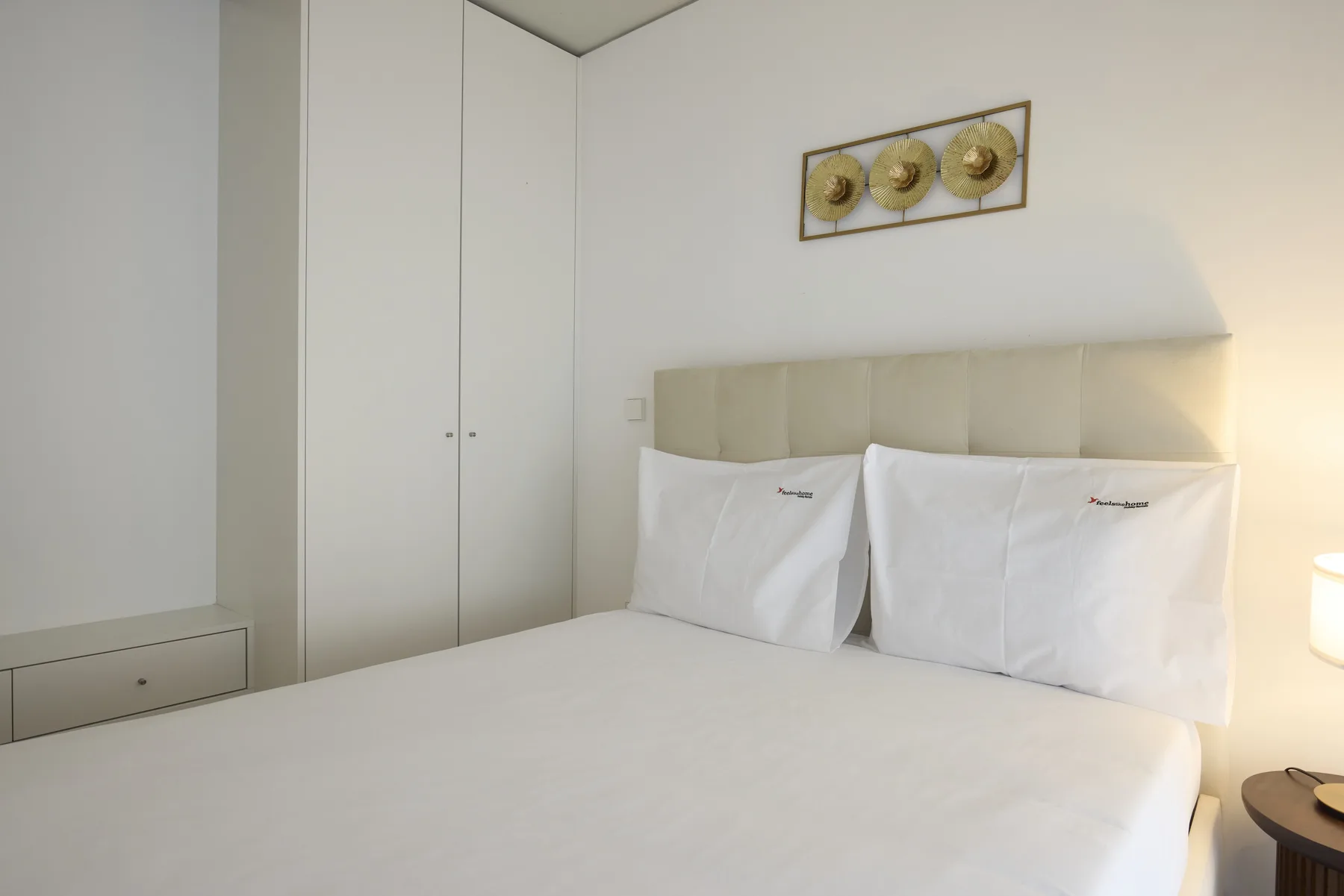 A bright bedroom with a bed, upholstered headboard, and framed wall decoration.