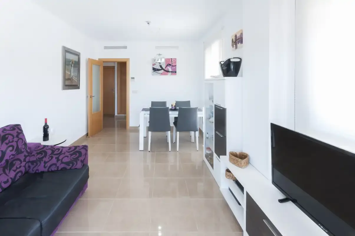 A bright living and dining area with seating, a dining table, and a television.