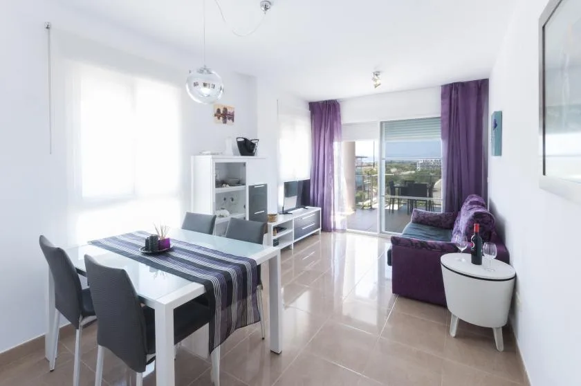Una luminosa zona de estar y comedor con una mesa y asientos morados.