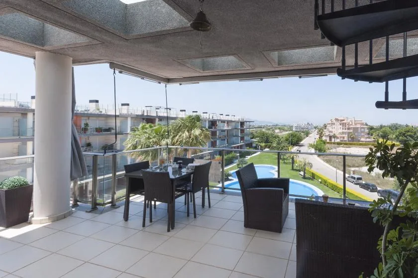 Una terraza cubierta con asientos al aire libre da a una piscina y edificios cercanos.