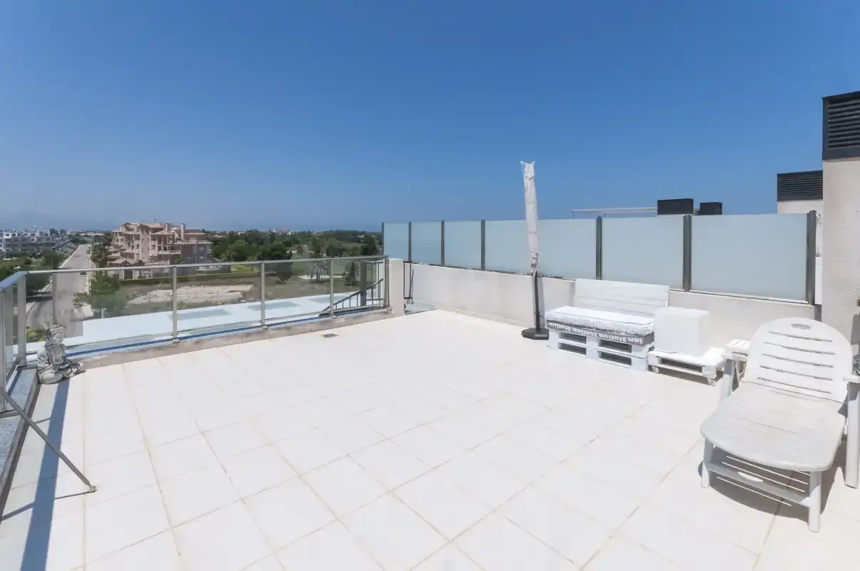 A sunny rooftop terrace with outdoor seating and glass railings.