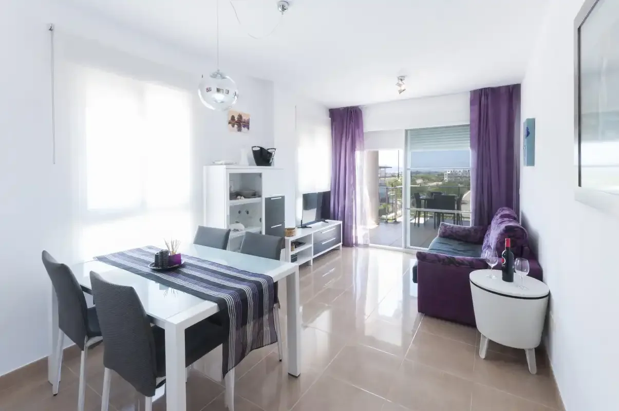 A bright living and dining room opens onto a balcony through sliding glass doors.