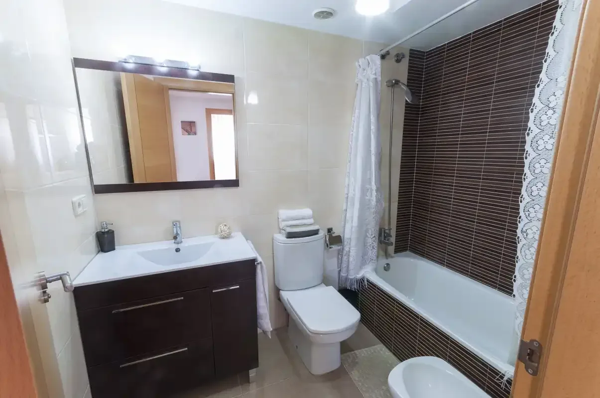 A bathroom with a sink, toilet, and bathtub beside a dark tiled wall.