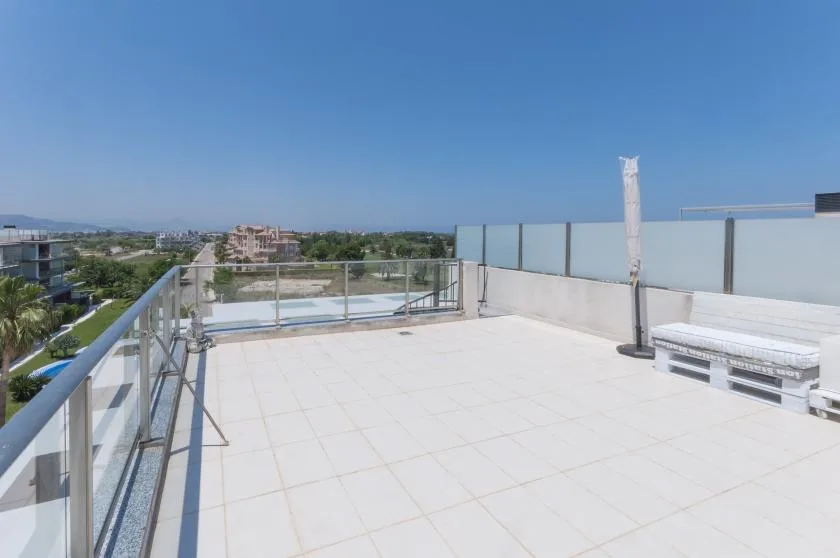 A spacious rooftop terrace with pale tiled flooring and glass railings.