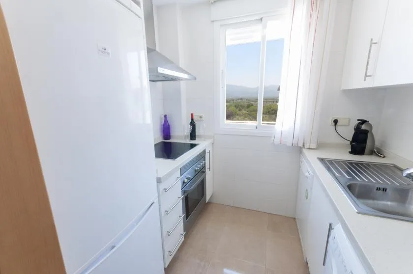 A bright galley kitchen with white cabinets and a window overlooking greenery.