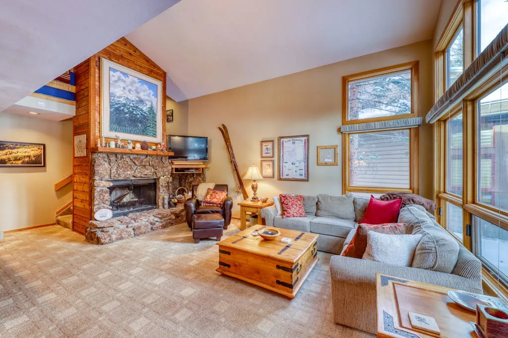 A living room with a stone fireplace, seating, and large windows.