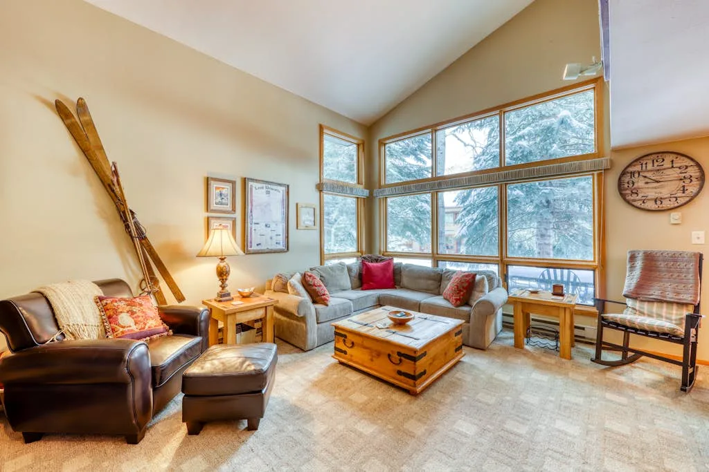A living room with a sectional sofa, armchair, and large windows.