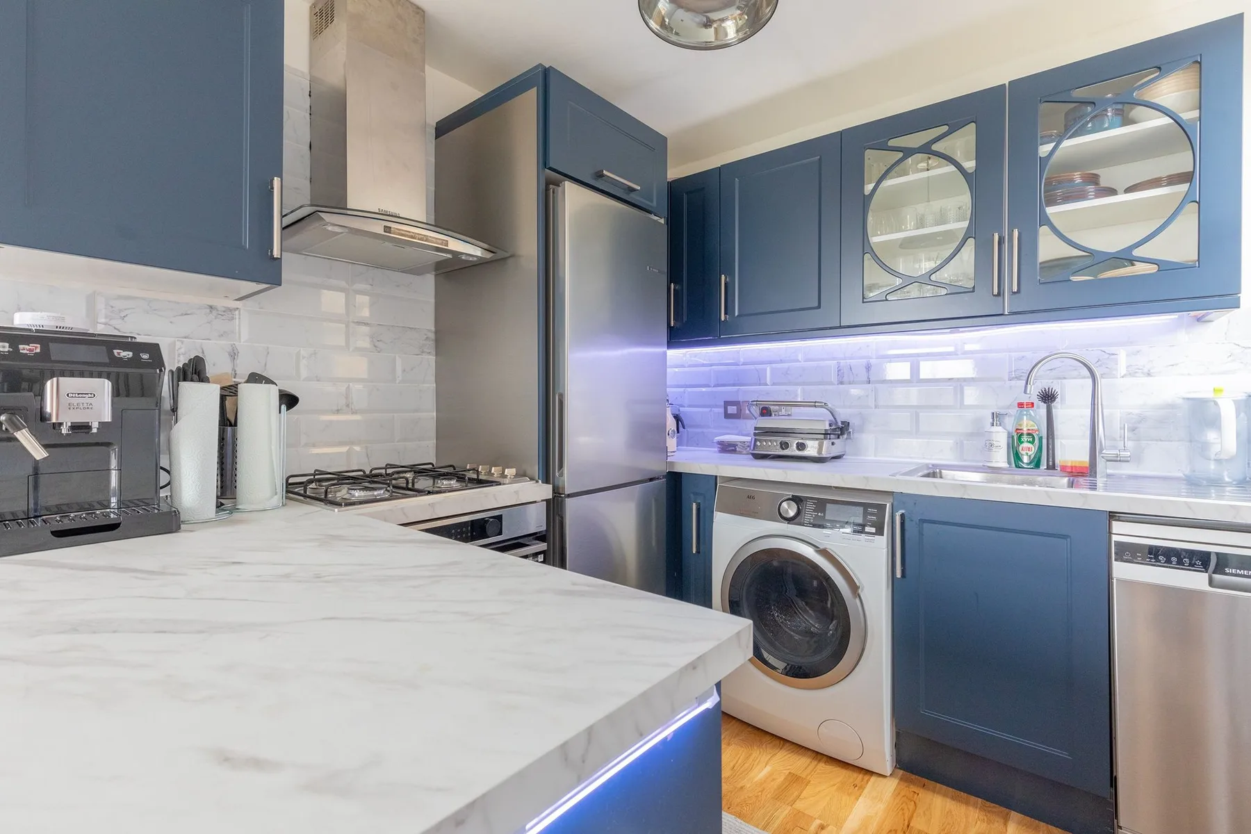 Una cocina moderna con gabinetes azules, una lavadora y una encimera con diseño de mármol.