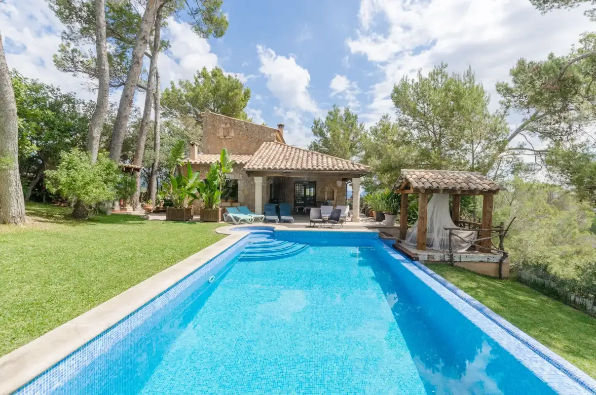 A swimming pool in front of a house, surrounded by trees and lawn.