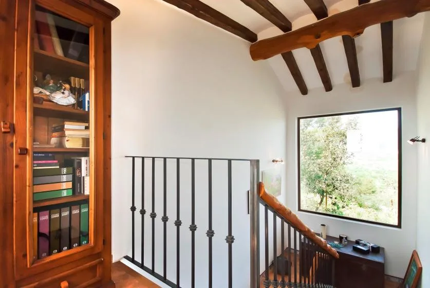A stair landing with a wooden bookcase, dark railing, and a large window.