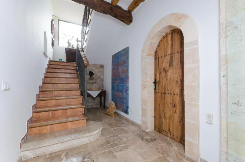 A stone-floored interior with a wooden staircase and an arched wooden door.