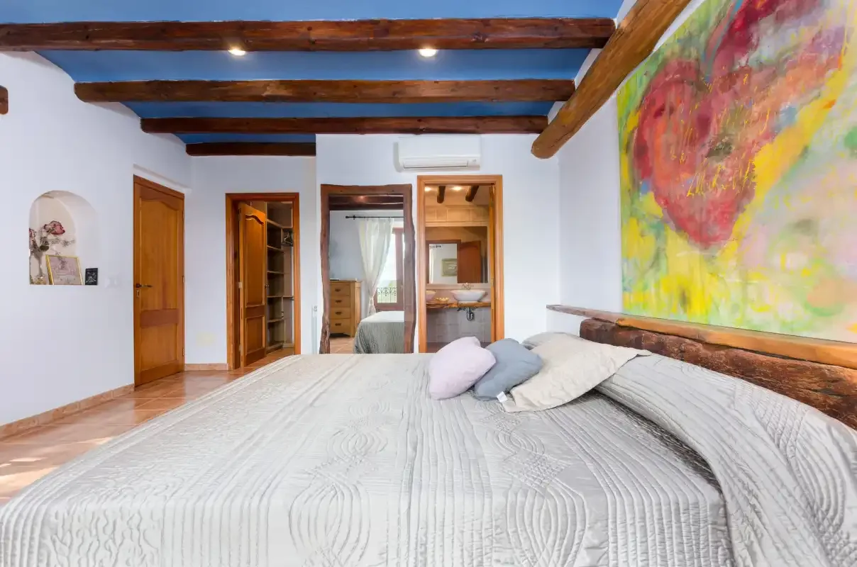 A bedroom with a large bed beneath exposed wooden ceiling beams.