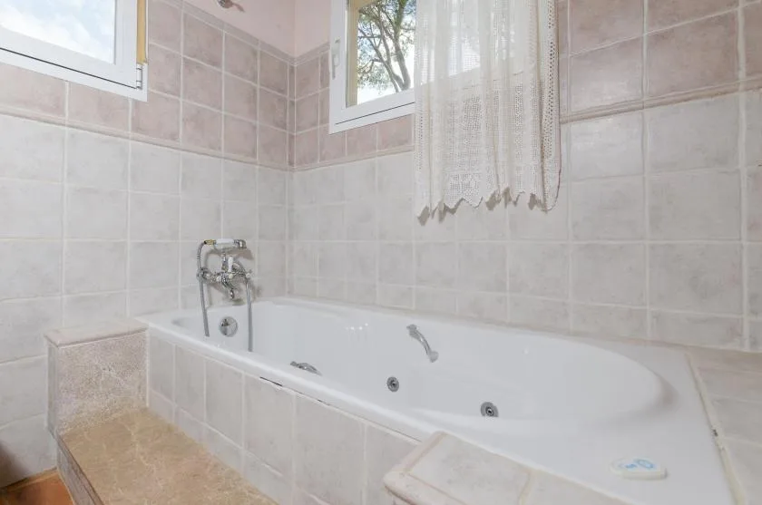 A tiled bathroom with a bathtub beneath two windows.