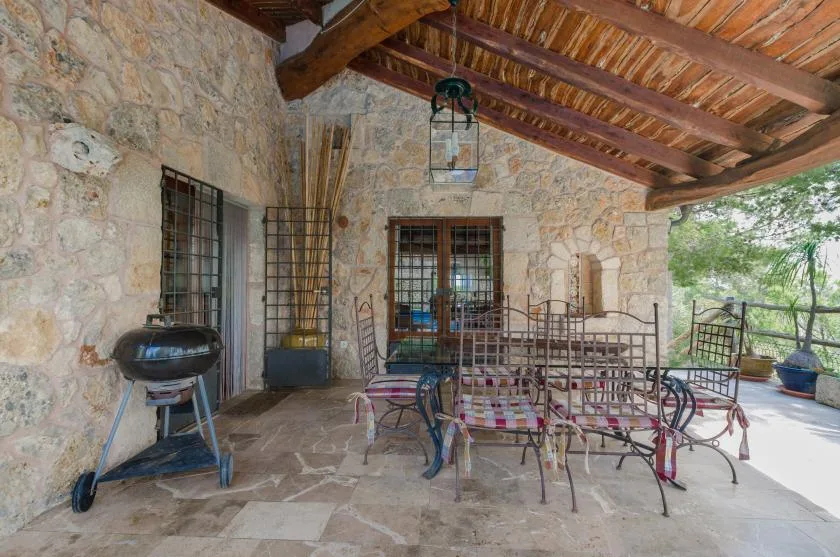 A covered stone patio with metal seating and a barbecue grill.
