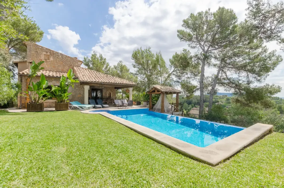 A swimming pool beside a stone house, surrounded by lawn and trees.