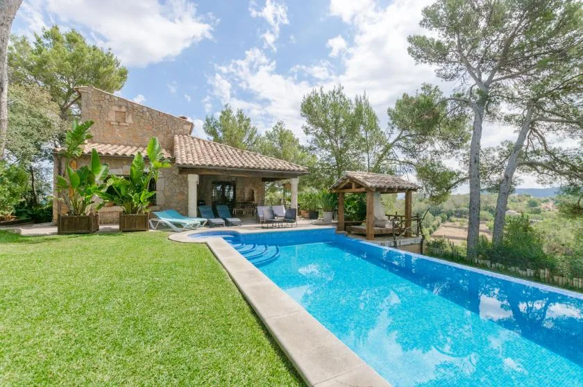 A swimming pool beside a stone house, with trees and lawn around it.