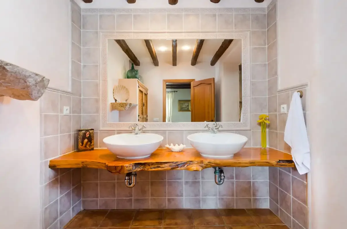 A tiled bathroom features two white sinks on a wooden counter beneath a large mirror.