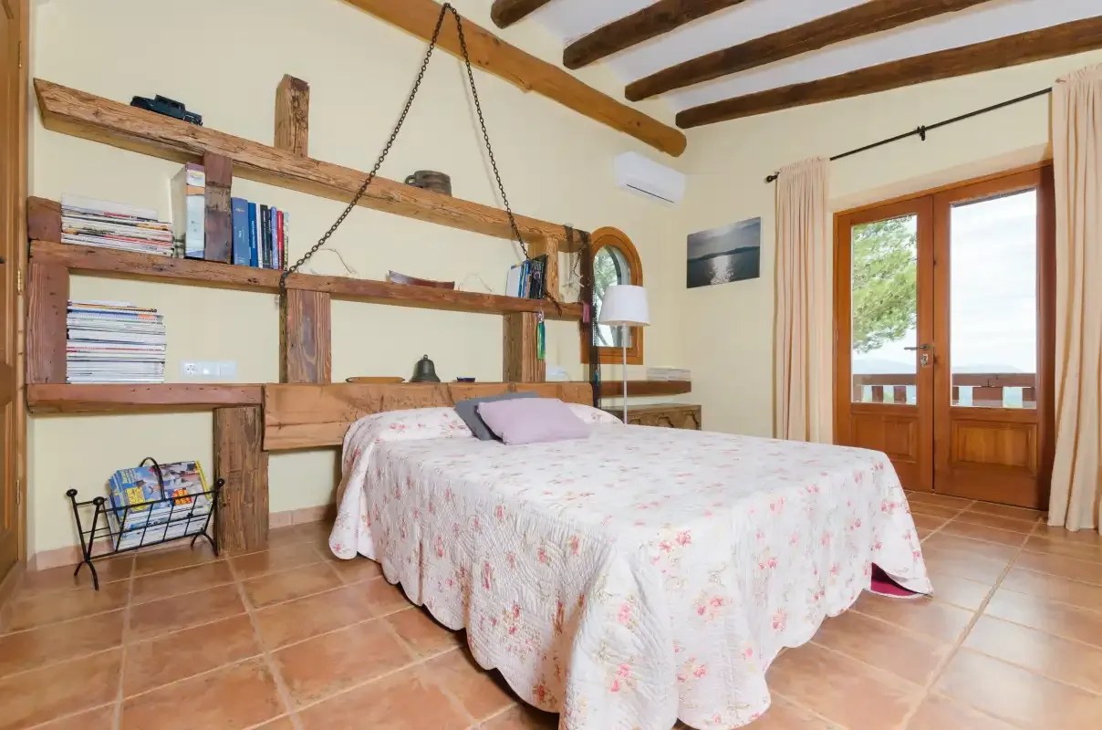 A bedroom with a bed beneath rustic wooden ceiling beams.
