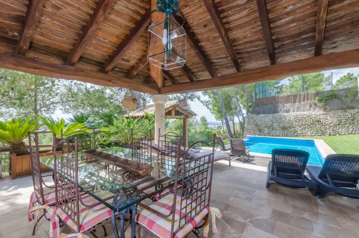 A shaded outdoor dining area overlooks a swimming pool and surrounding greenery.