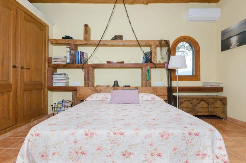 A bedroom with a floral bedspread and wooden shelving behind the bed.