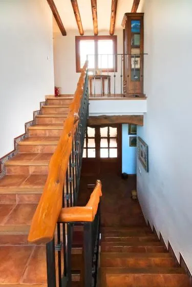 A stairwell with terracotta steps, a wooden handrail, and a window above.
