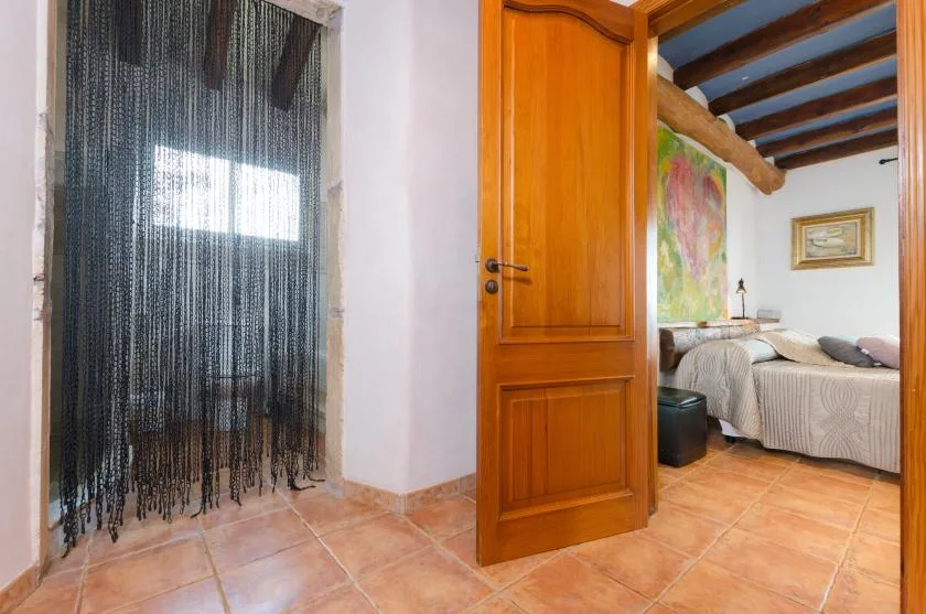 A bedroom is visible through an open wooden door, with a bed beneath exposed ceiling beams.