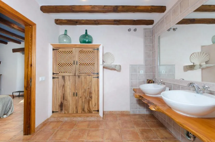 A tiled bathroom with wooden vanities, countertop sinks, and a wooden cabinet.