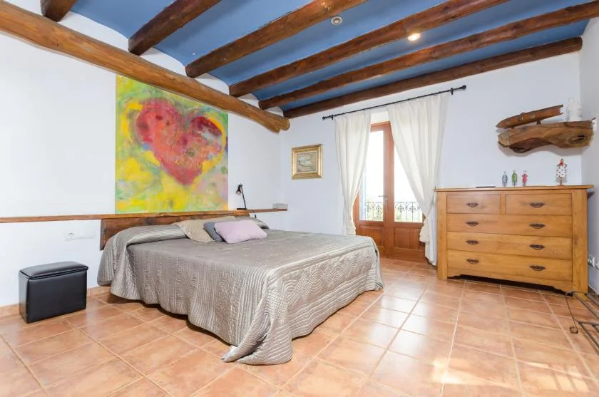 A bedroom with a bed, wooden ceiling beams, and a dresser.
