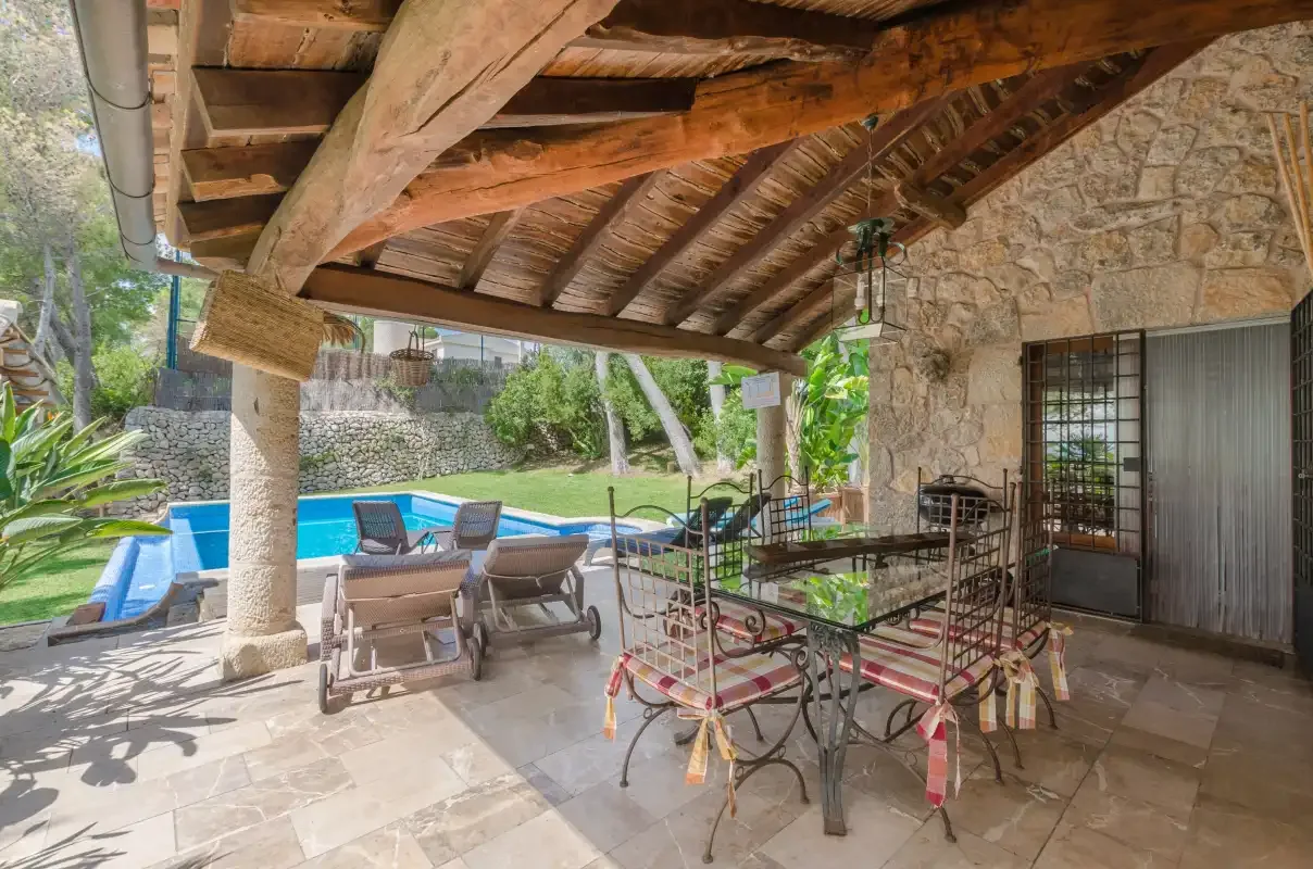 A covered outdoor dining and seating area overlooks a swimming pool.